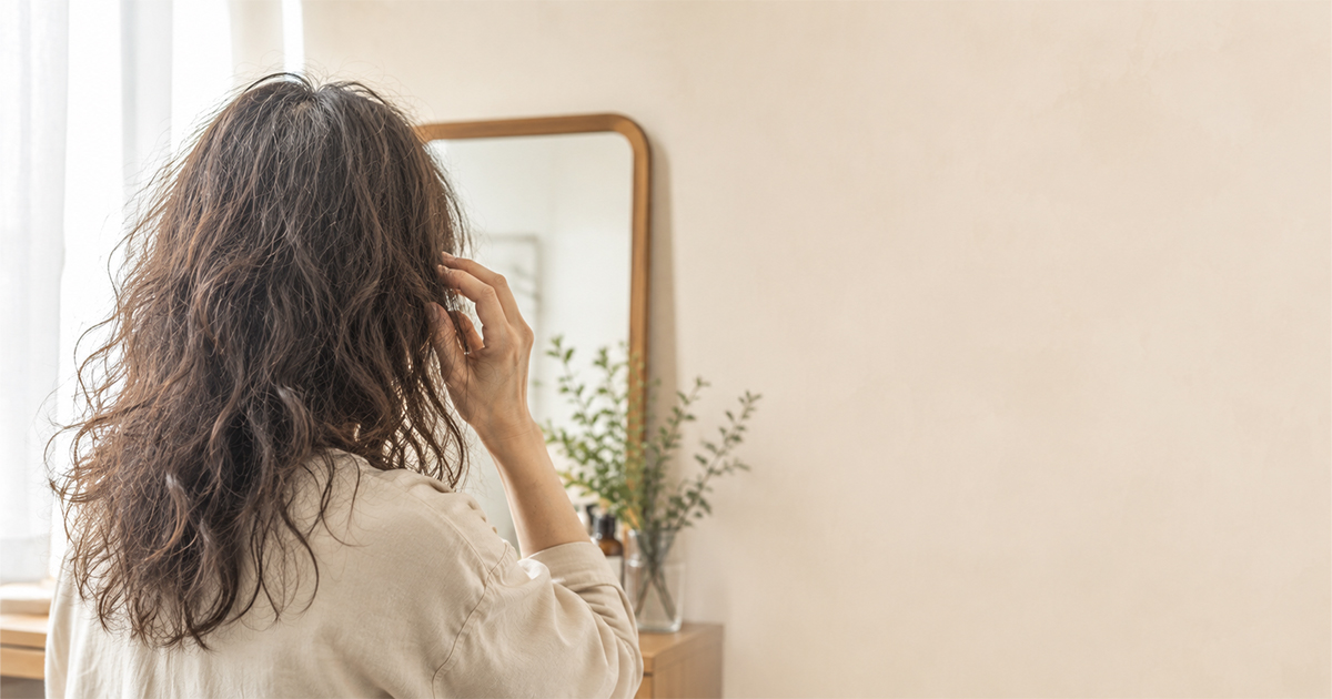 くせ毛カットの失敗に悩む女性が鏡の前で髪を触っている様子